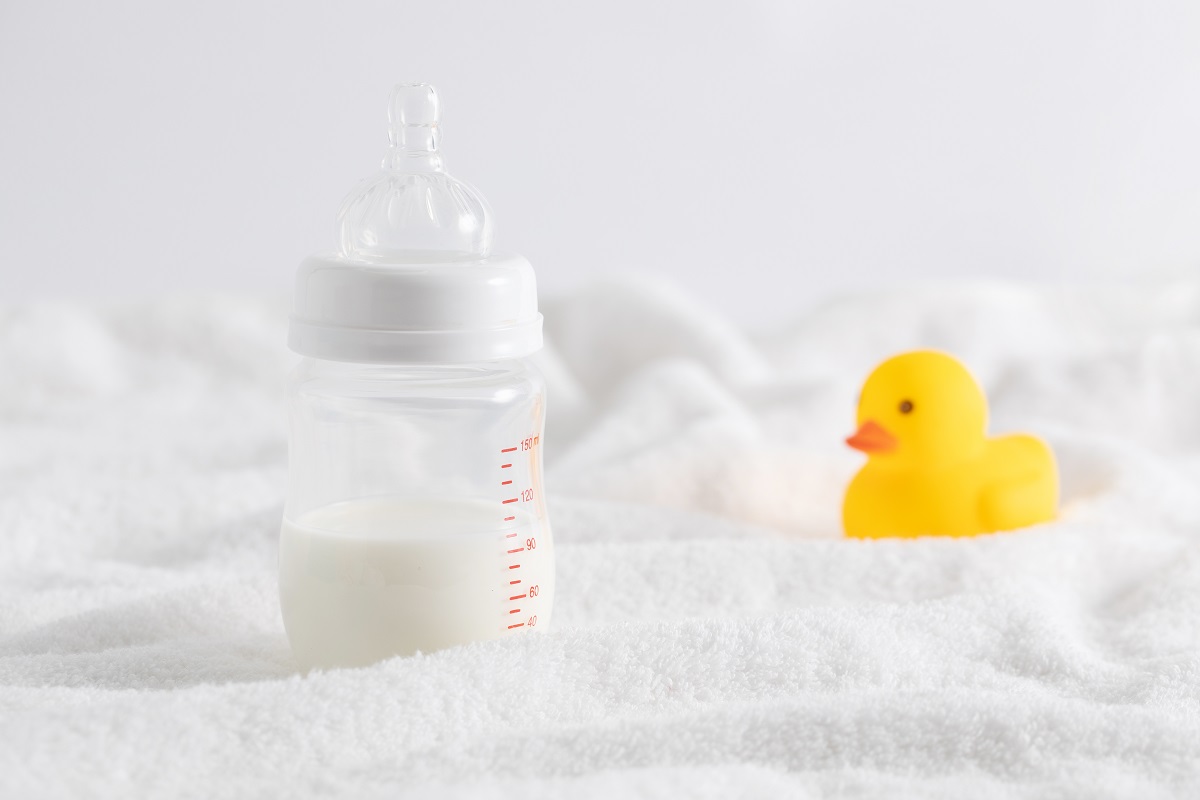 Closeup of a bottle full of milk next to a duck toy on a white surface
